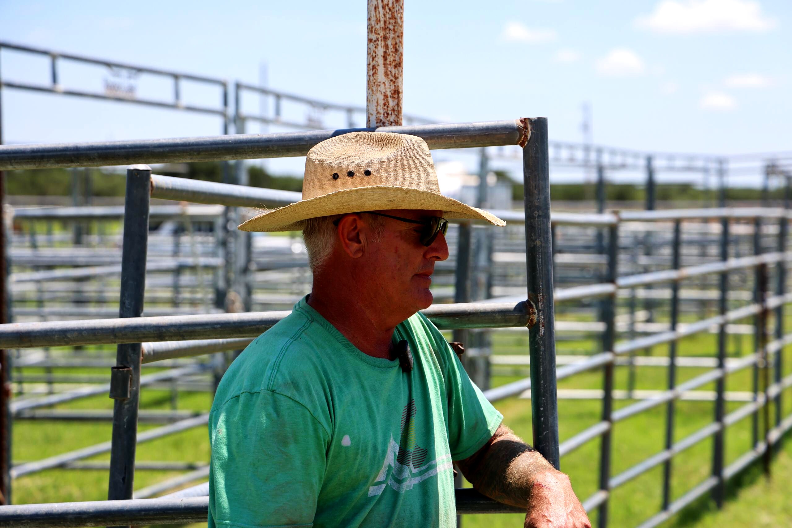 Man in a straw hat leaning on arena pipe fencing