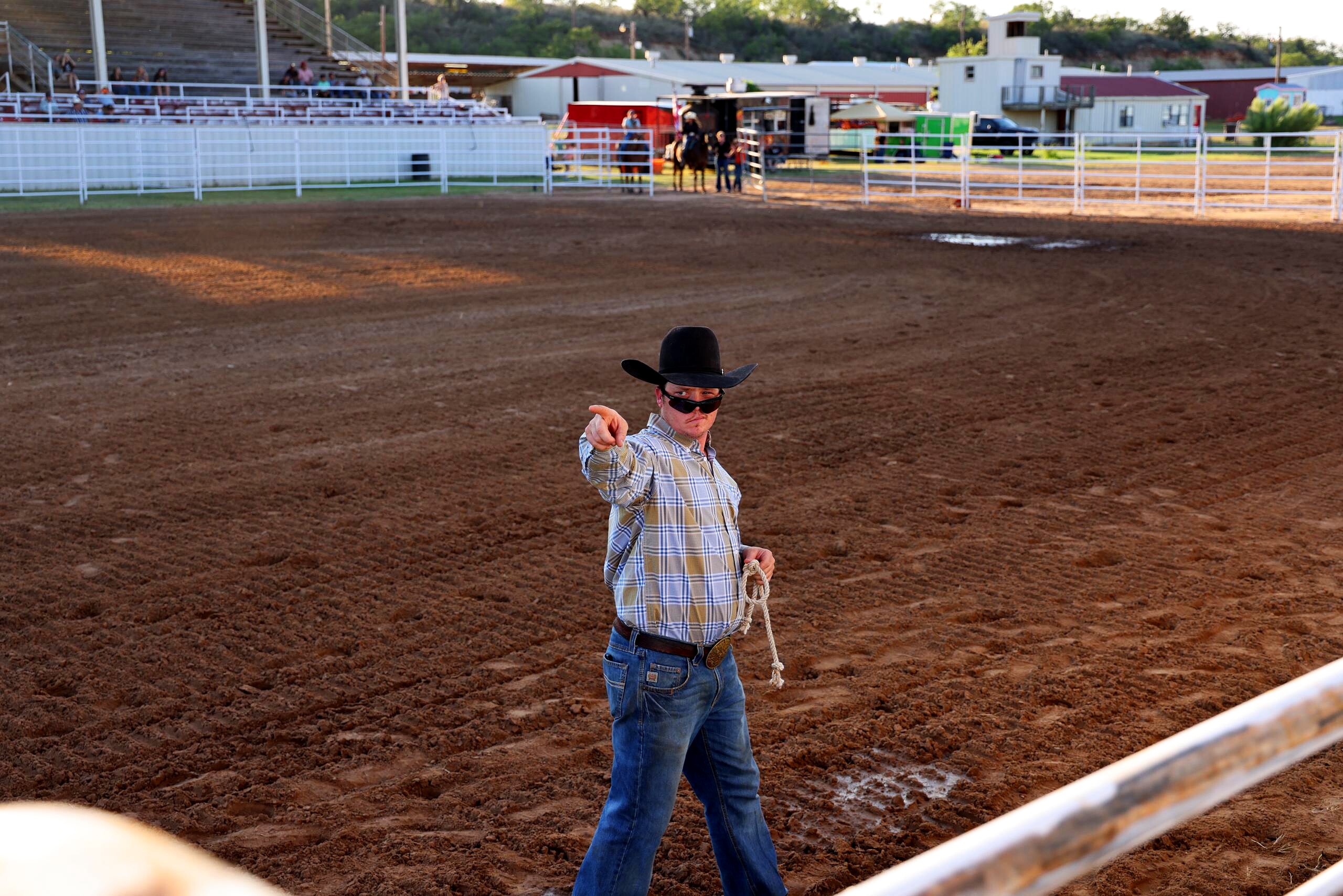 Cowboy in a black hat pointing from inside the rodeo arena