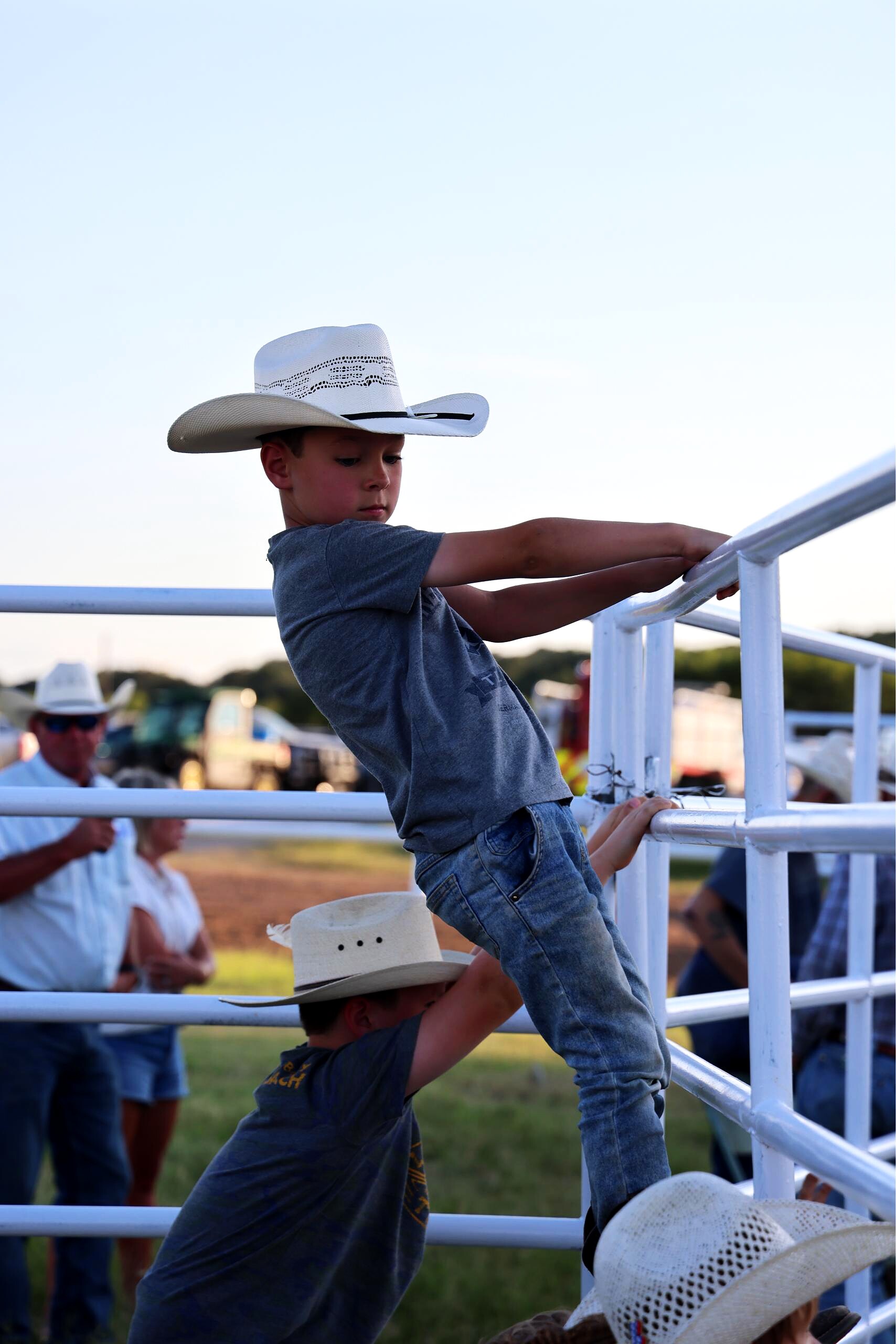 Young boy in a white cowboy hat climbing arena railing