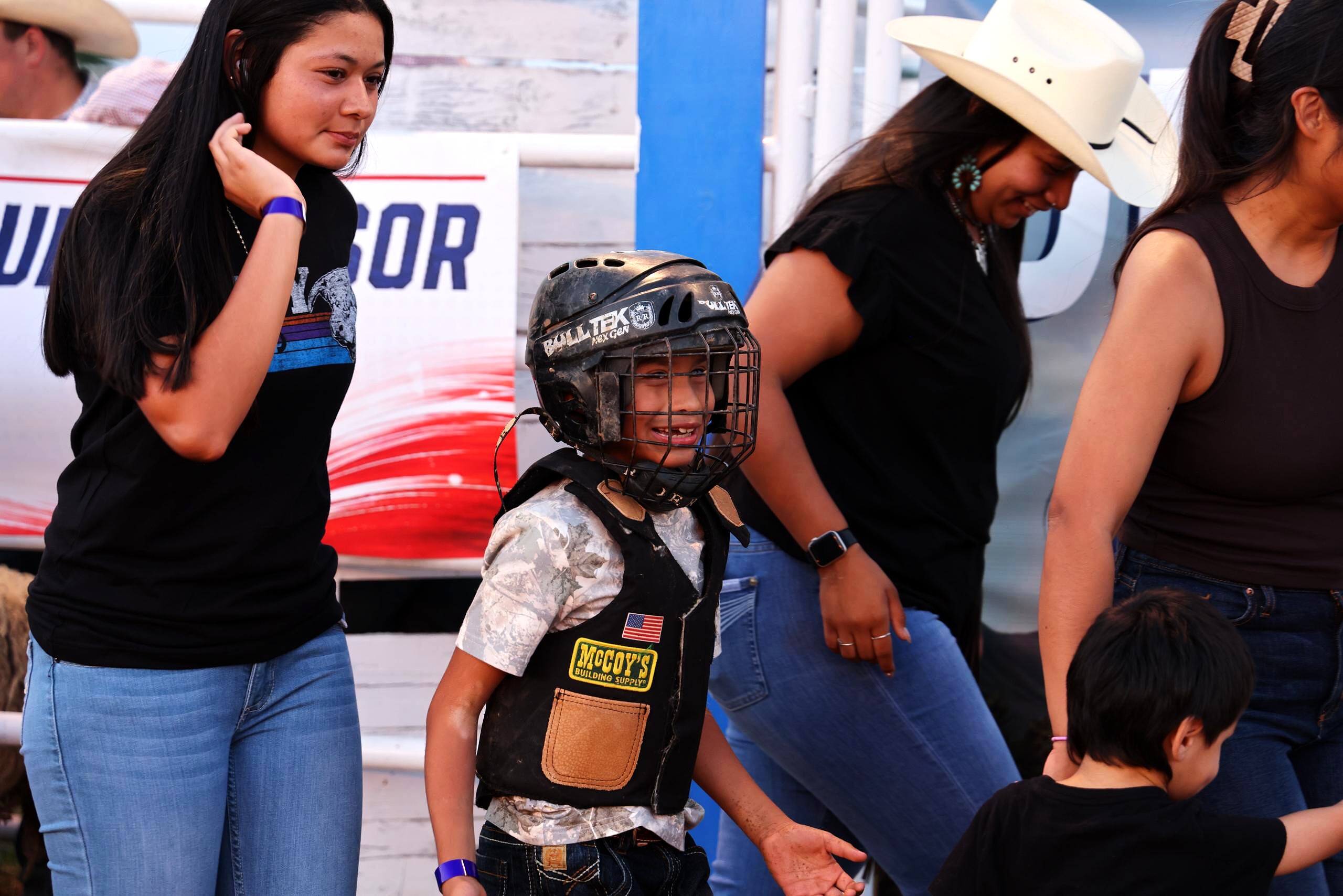 Young mutton busting rider smiling in protective gear beside family near the arena