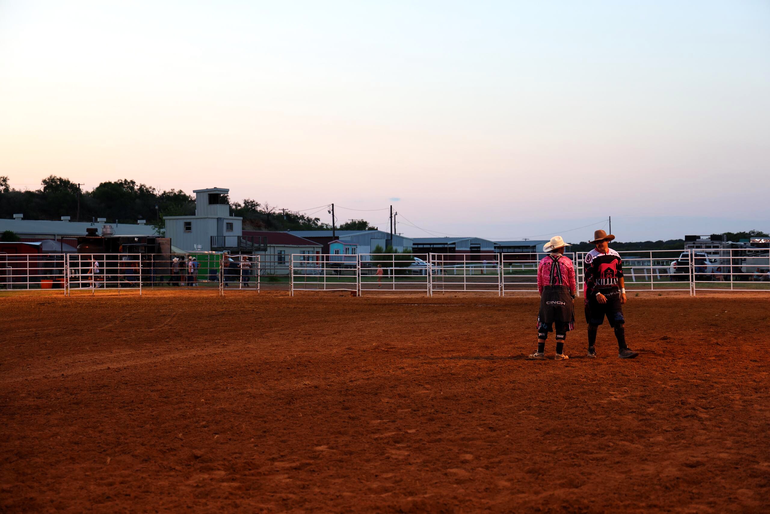 Two rodeo crew members walking across the arena at sunset