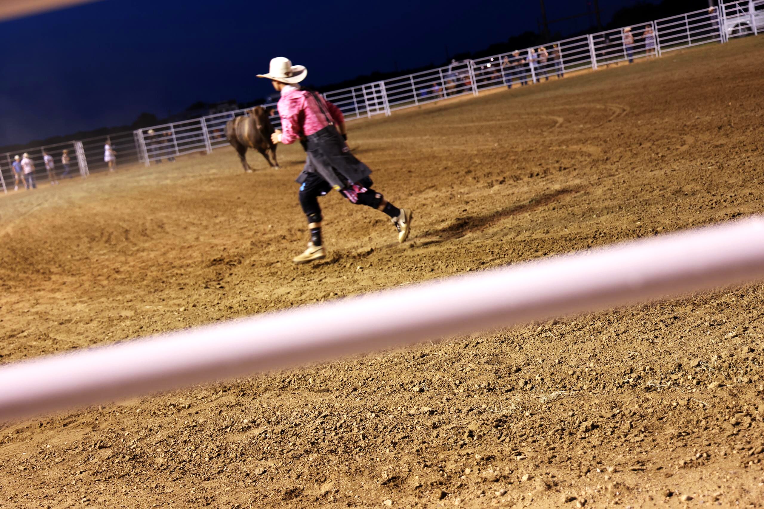 Young rodeo participant running across the night arena toward a bull
