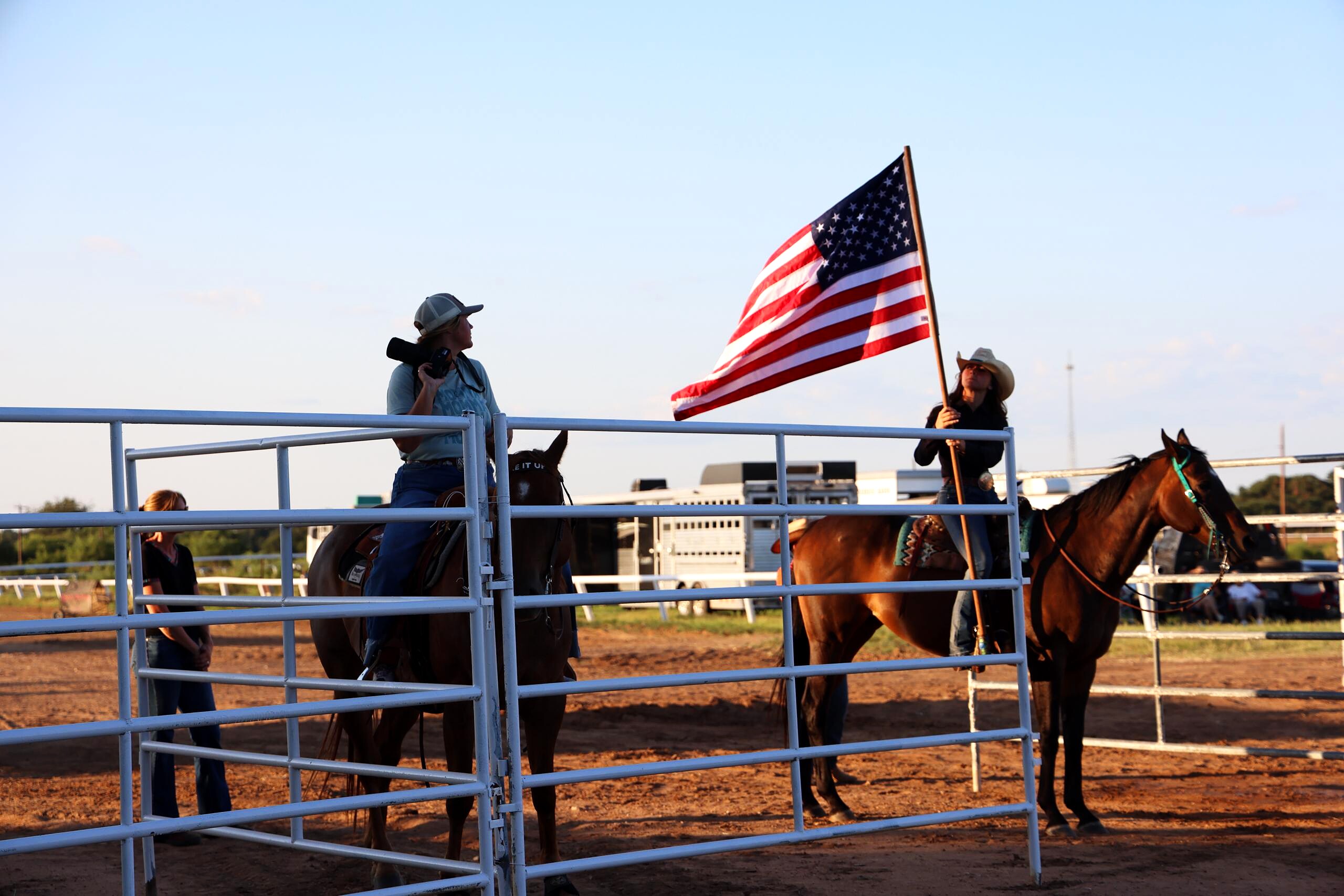 Rider carrying an American flag on horseback beside the arena rail