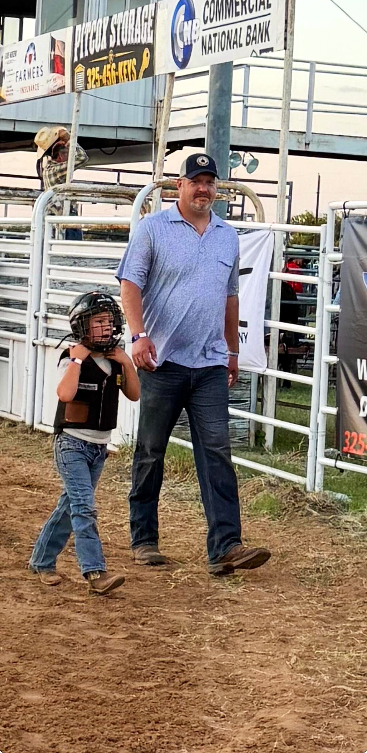 Adult and young rider walking through the rodeo grounds near arena gates
